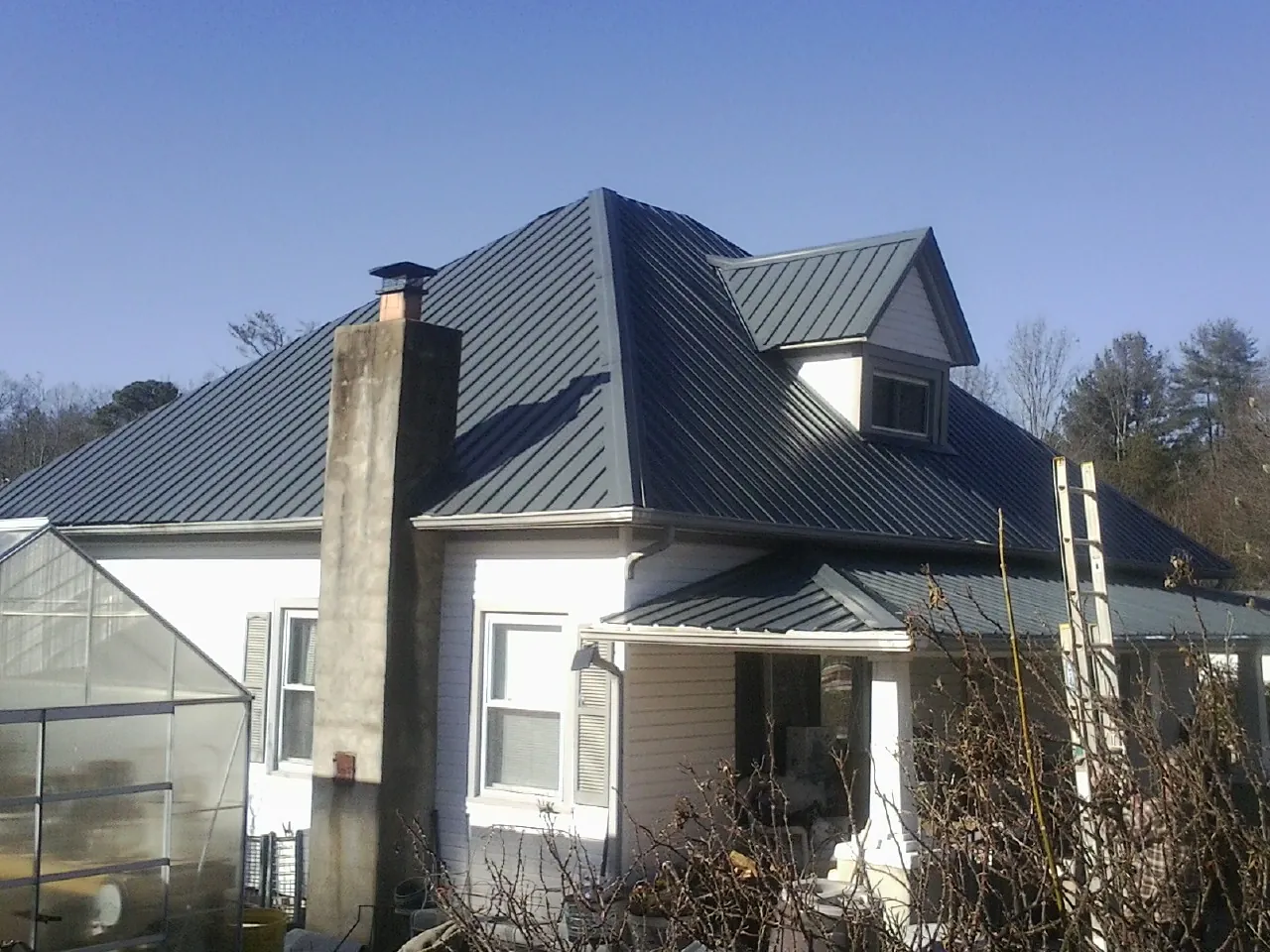 Dark blue standing seam metal roof on a white farmhouse with dormer — Slate & Tile Roof Repair by Roofing Brothers in Midfield