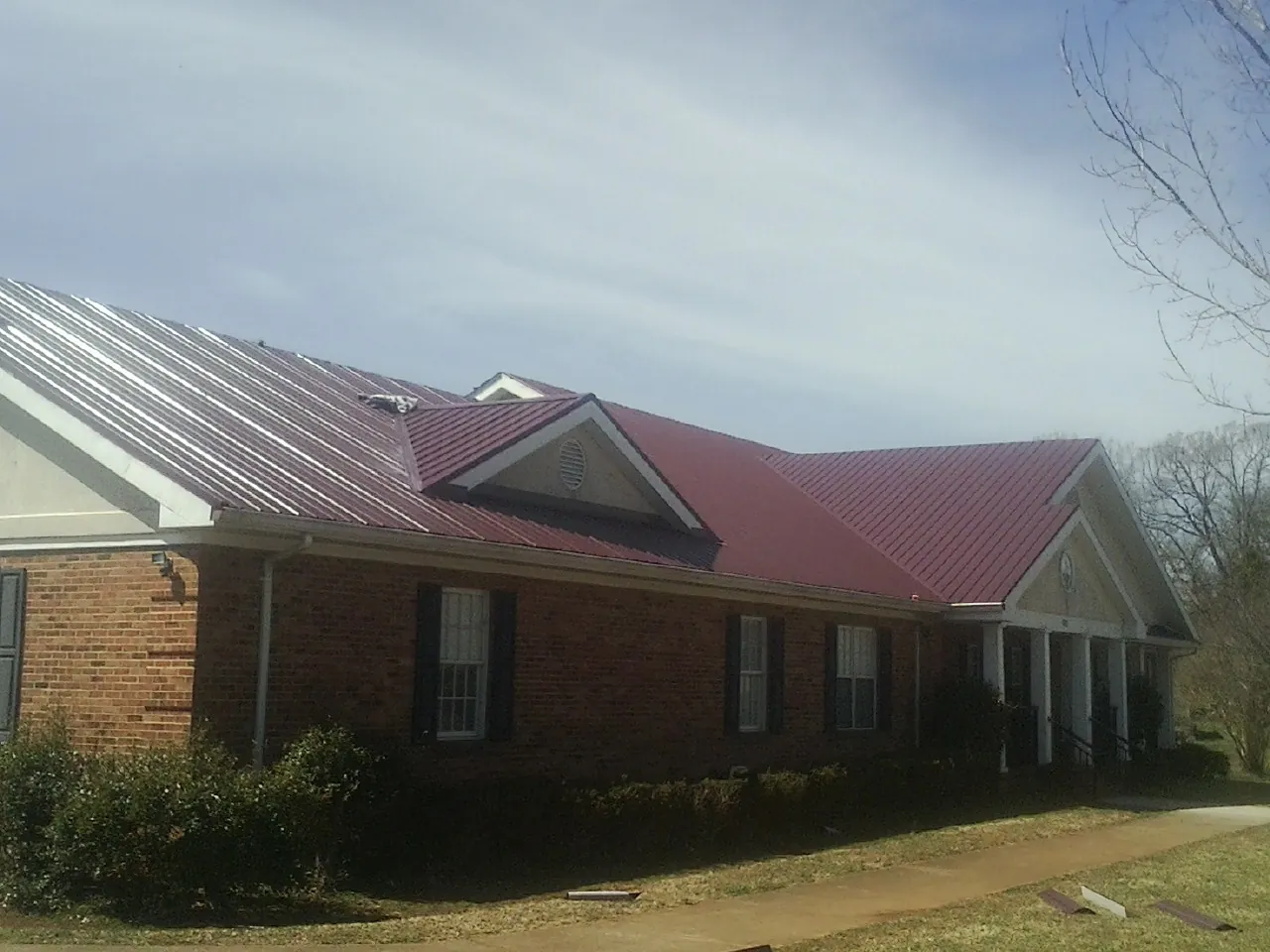 Red metal roof with gabled entries on a long brick building, from a Hail Damage Roof Repair job in Midfield