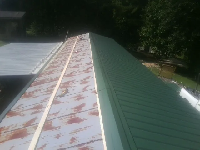 Old rusted panels beside newly installed green metal roofing — Wind Damage Roof Repair by Roofing Brothers in Midfield