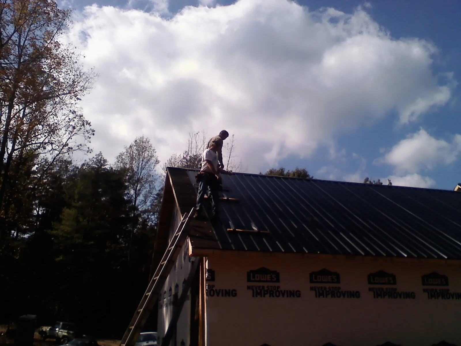 Roofer fastening dark metal panels high against a cloudy sky, from a Roof Inspection job in Midfield